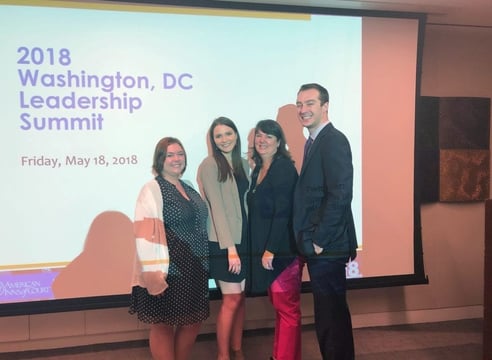 Three female and one male professionals line up in front of a conference presentation.